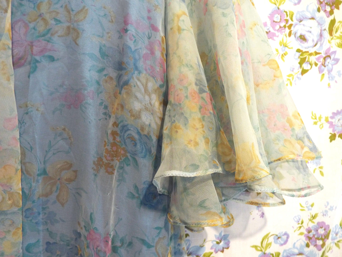 1970s Maxi Dress (S-M) with light blue floral patterned fabric and puffy sleeves, against patterned fabric with blue and purple roses.