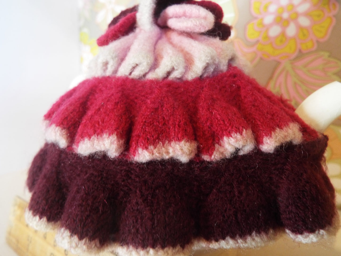 Tiny Frilly Vintage Tea Cosy with frills in different shades of pink against warm floral backdrop.