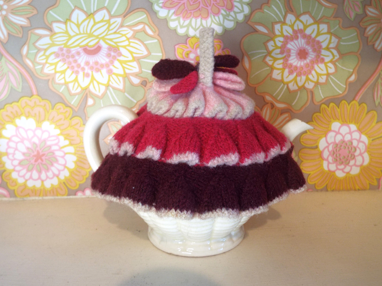 Tiny Frilly Vintage Tea Cosy with frills in different shades of pink against warm floral backdrop.