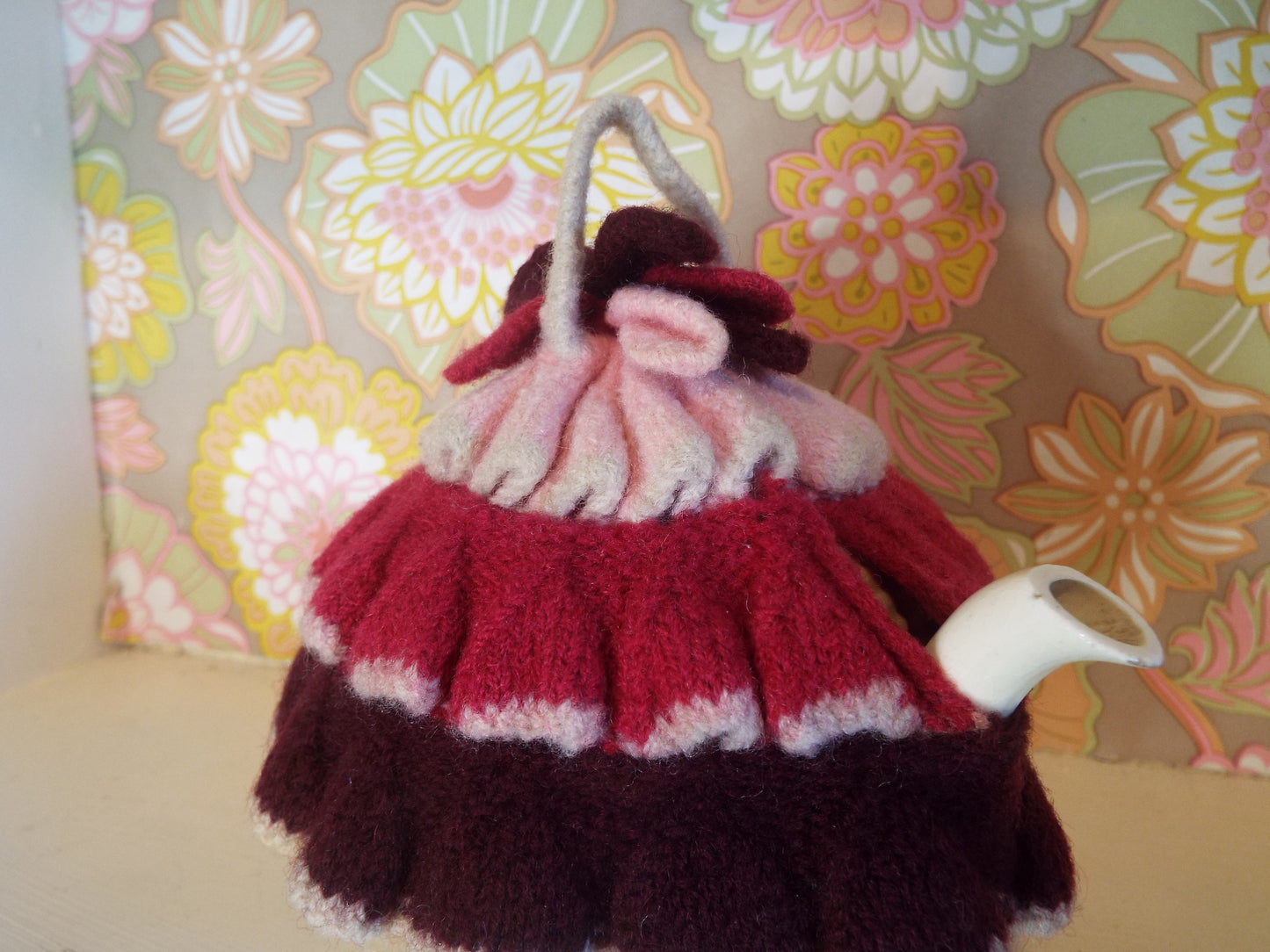 Tiny Frilly Vintage Tea Cosy with frills in different shades of pink against warm floral backdrop.