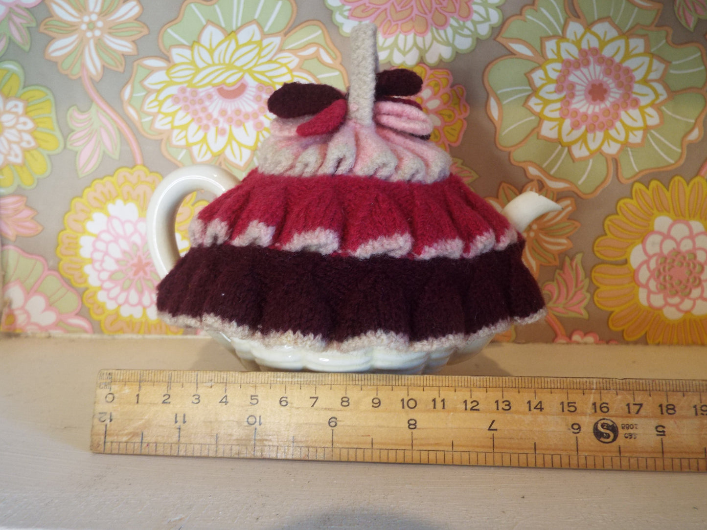 Tiny Frilly Vintage Tea Cosy with frills in different shades of pink against warm floral backdrop.