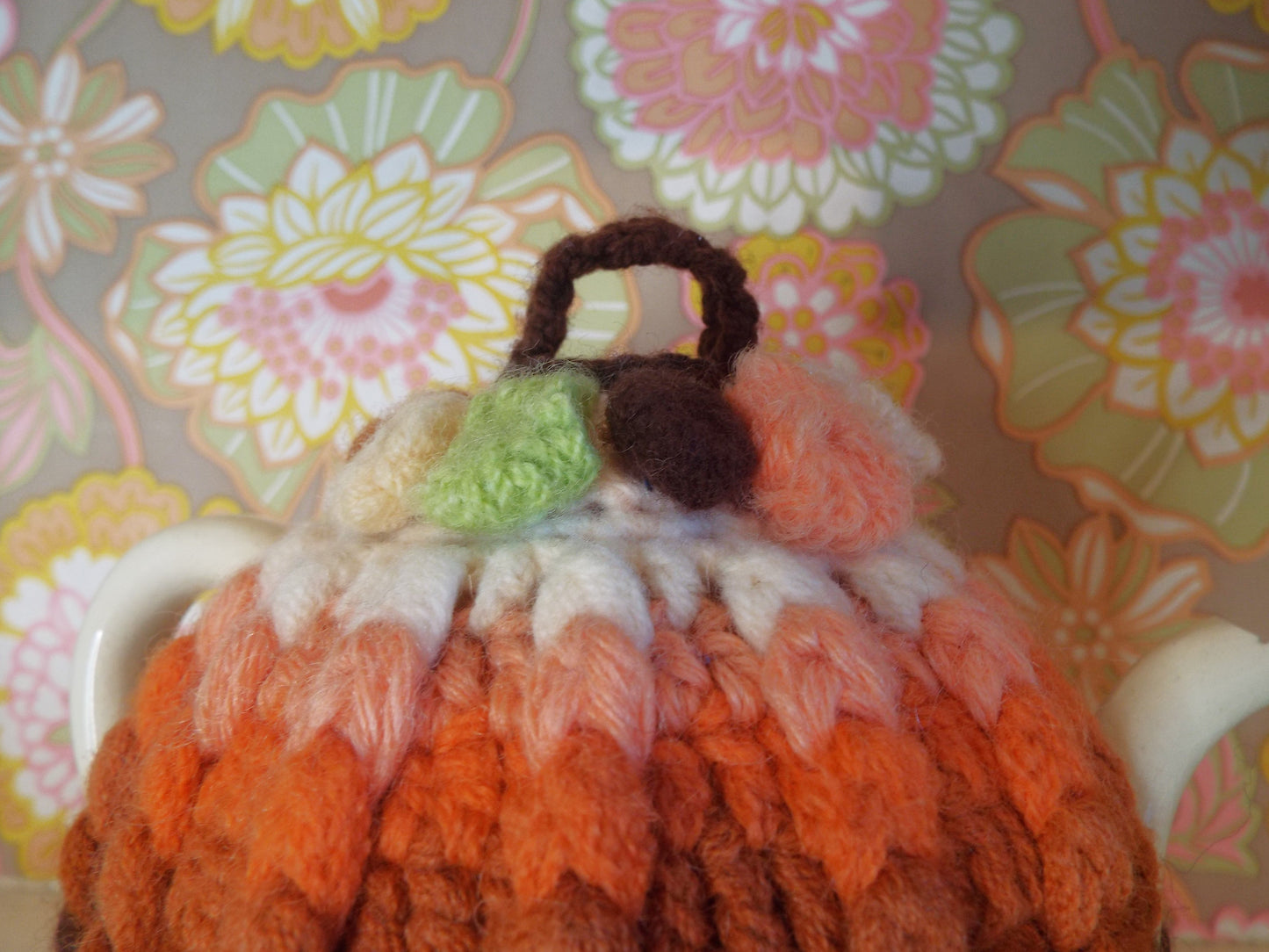 Small Vintage Tea Cosy with brown and orange ombre design against warm floral backdrop.