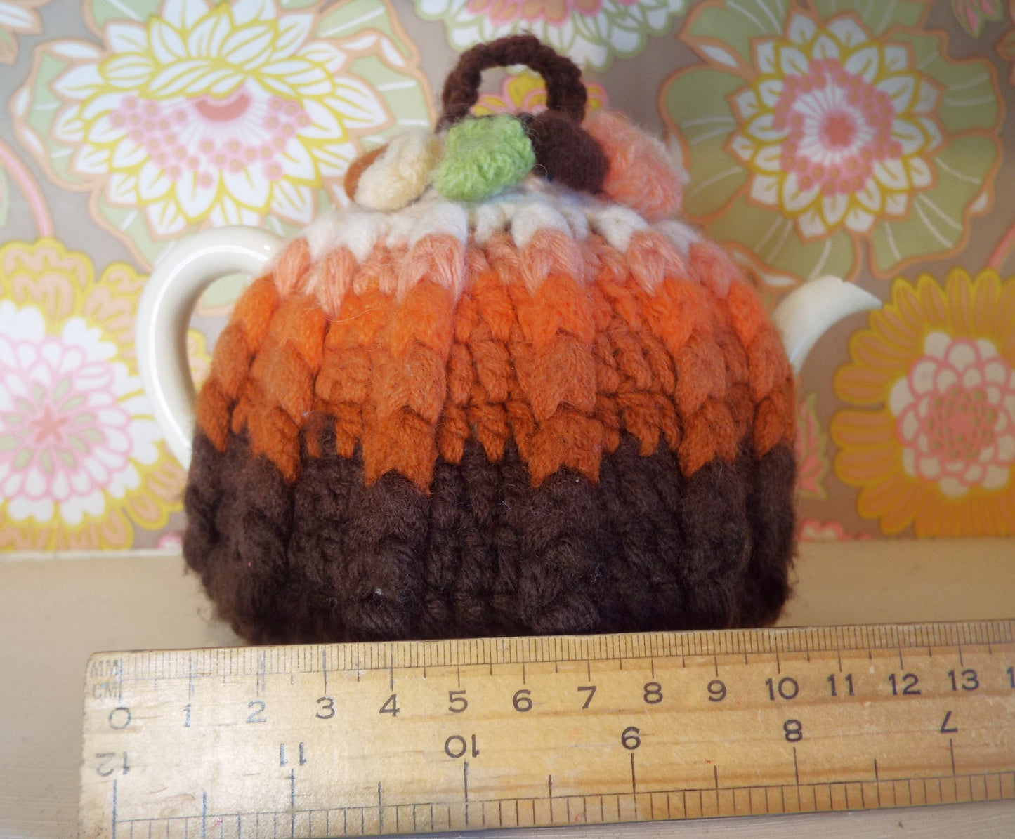 Small Vintage Tea Cosy with brown and orange ombre design against warm floral backdrop.