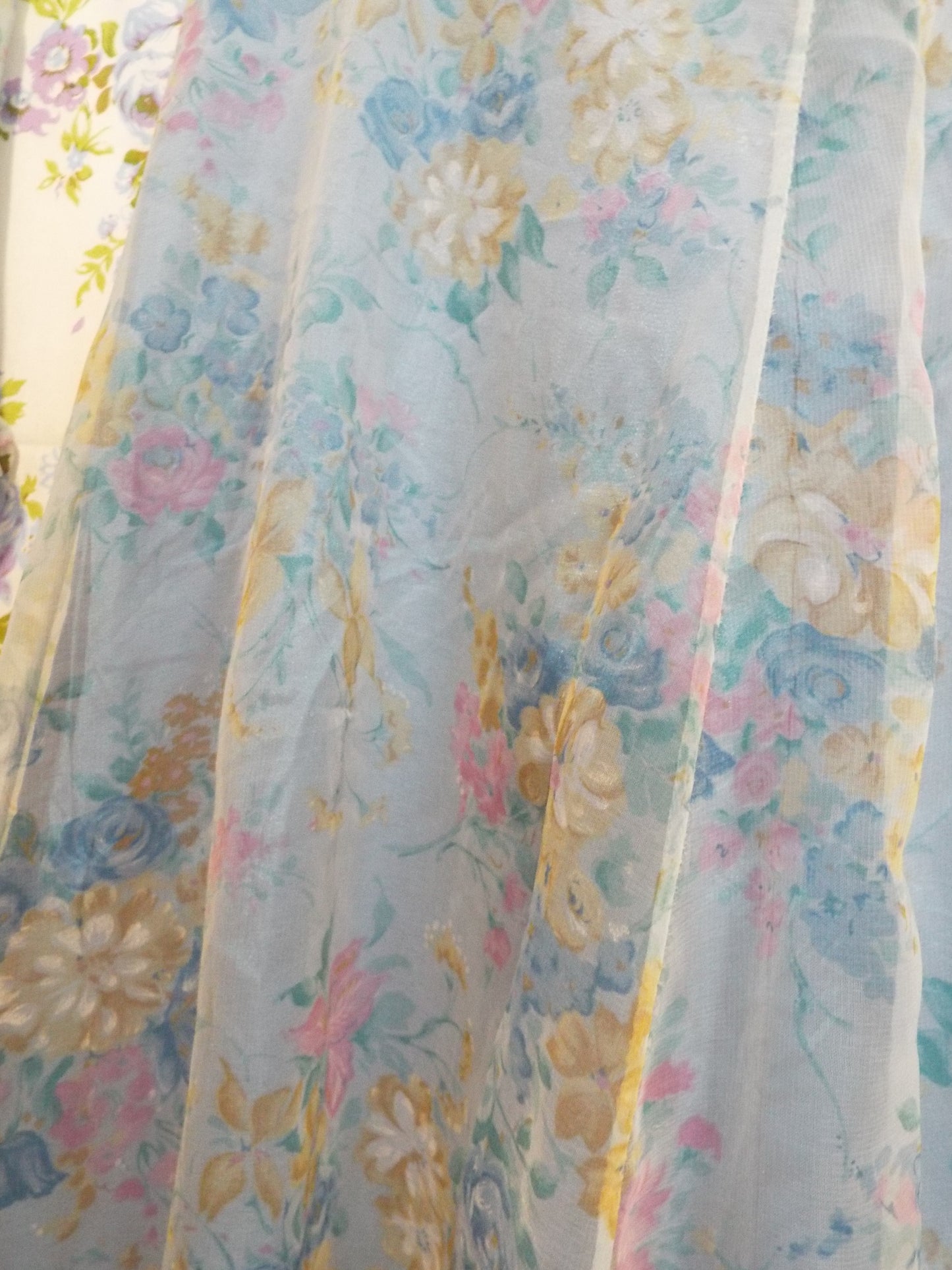 Close-up of pull in fabric on 1970s Maxi Dress (S-M) with light blue floral patterned fabric and puffy sleeves, against patterned fabric with blue and purple roses.