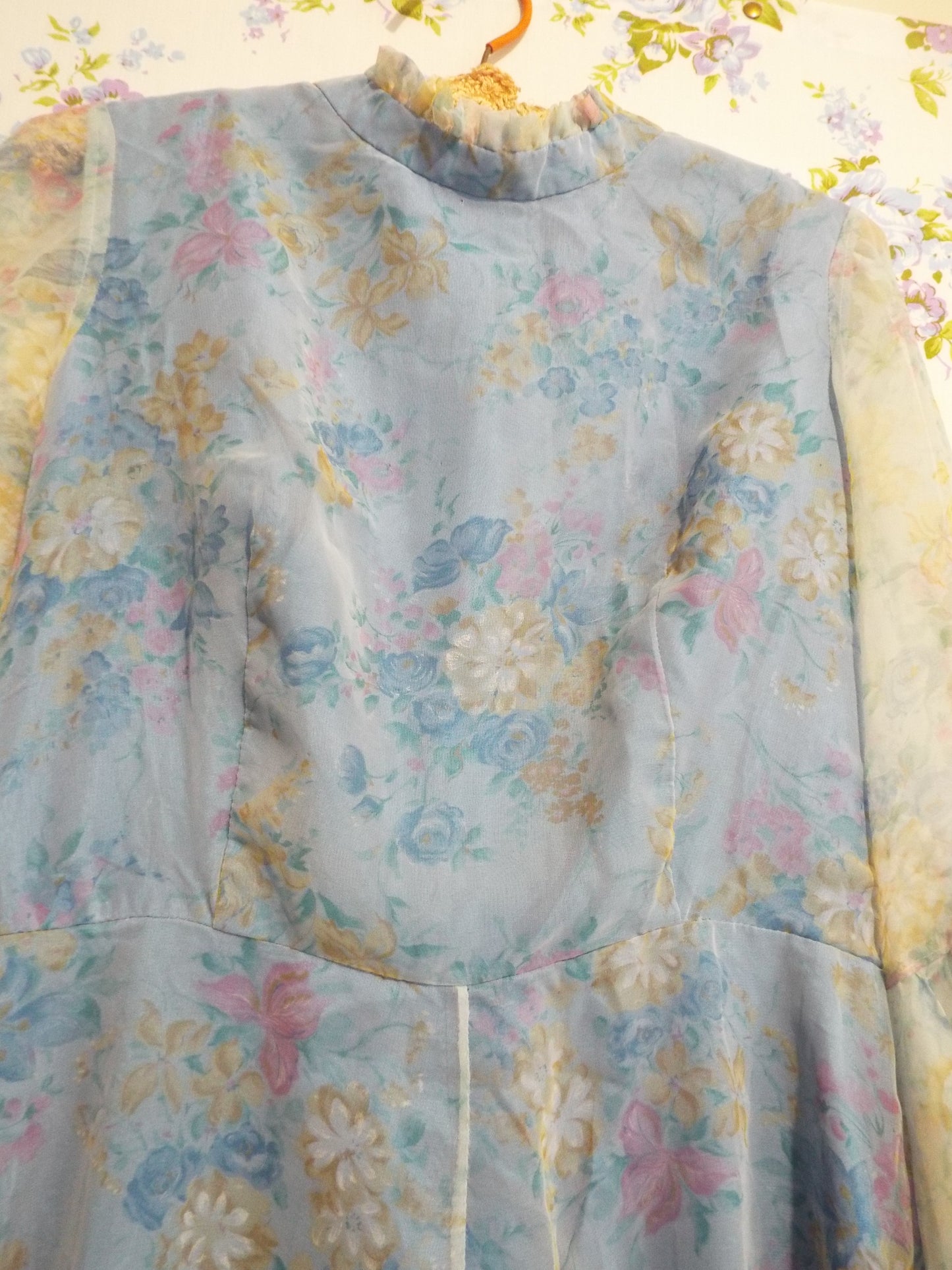 1970s Maxi Dress (S-M) with light blue floral patterned fabric and puffy sleeves, against patterned fabric with blue and purple roses.