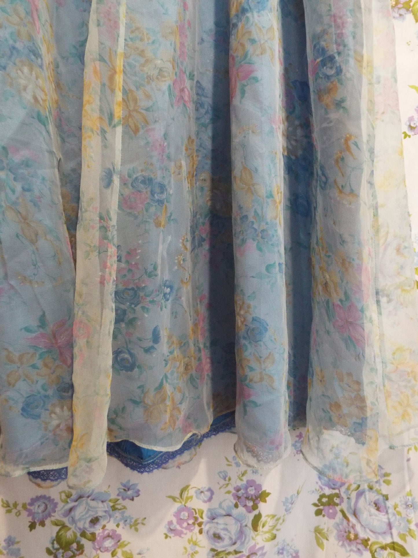1970s Maxi Dress (S-M) with light blue floral patterned fabric and puffy sleeves, against patterned fabric with blue and purple roses.