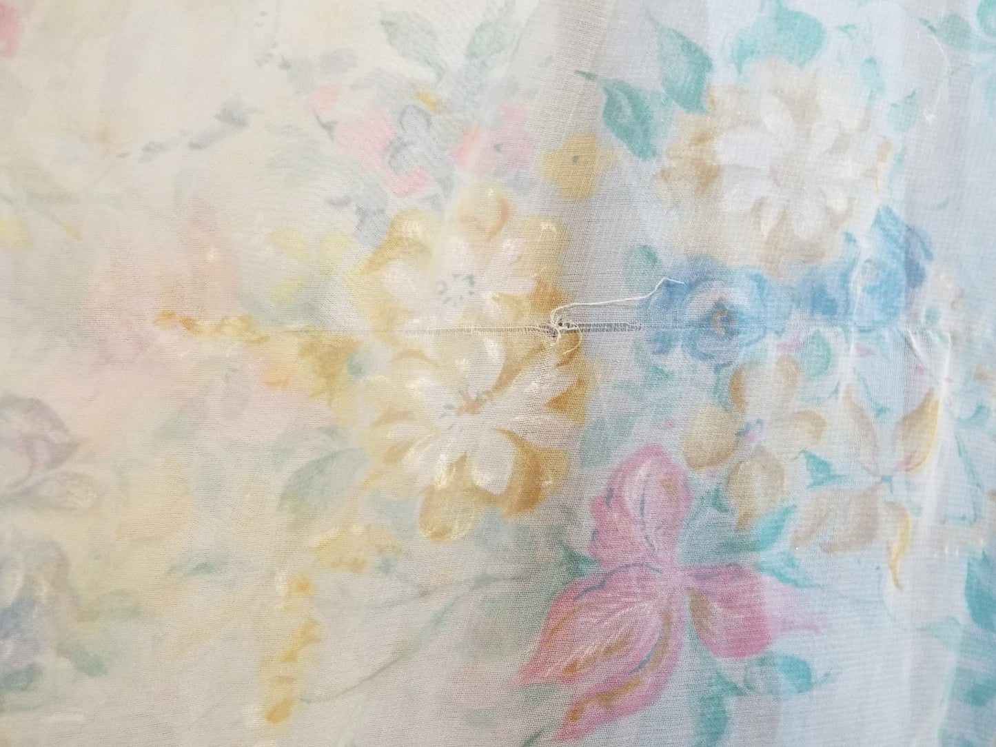 Close-up of pull in fabric on 1970s Maxi Dress (S-M) with light blue floral patterned fabric and puffy sleeves, against patterned fabric with blue and purple roses.