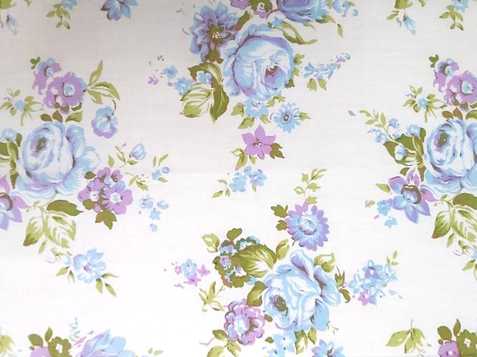 A vintage sheet with a blue and purple floral rose pattern with green leaves.