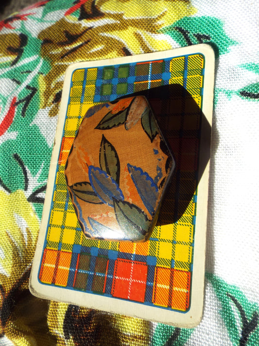 Vintage Brooch - Painted Wood - Art Deco Style on tartan card, against leafy backdrop.